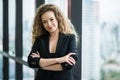 Young beautiful business woman standing arms crossed near window in office. Smiling sexy lady confident in black suited