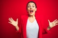 Young beautiful business woman standing over red isolated background celebrating crazy and amazed for success with arms raised and Royalty Free Stock Photo