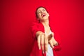 Young beautiful business woman standing over red isolated background laughing at you, pointing finger to the camera with hand over Royalty Free Stock Photo