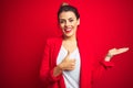 Young beautiful business woman standing over red isolated background Showing palm hand and doing ok gesture with thumbs up, Royalty Free Stock Photo