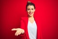 Young beautiful business woman standing over red isolated background smiling cheerful offering palm hand giving assistance and Royalty Free Stock Photo