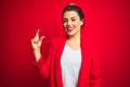 Young beautiful business woman standing over red isolated background smiling and confident gesturing with hand doing small size Royalty Free Stock Photo