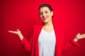 Young beautiful business woman standing over red isolated background smiling showing both hands open palms, presenting and Royalty Free Stock Photo