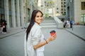 Beautiful business woman is going to work with coffee walking near office buildings. Portrait of a successful business woman holdi Royalty Free Stock Photo