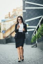 Young beautiful business woman walks next to an office building with documents and using the phone while distracted from Royalty Free Stock Photo