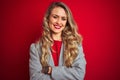 Young beautiful business woman wearing elegant jacket standing over red isolated background happy face smiling with crossed arms Royalty Free Stock Photo