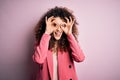 Young beautiful businesswoman with curly hair and piercing wearing elegant jacket doing ok gesture like binoculars sticking tongue Royalty Free Stock Photo