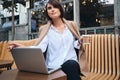 Young beautiful businesswoman dreamily working on laptop during coffee break in cafe on street