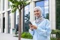 Young beautiful businesswoman in hijab walks in the city from outside the office building, woman uses an application on Royalty Free Stock Photo