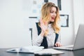 Young beautiful businesswoman manager with red lipstick works in her modern office, waving during online conference with client in Royalty Free Stock Photo