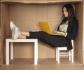Young beautiful businesswoman sitting in office cardboard box, legs on desk and working on computer Royalty Free Stock Photo