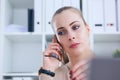 Beautiful young businesswoman speaking phone while using laptop and doing some paperwork.