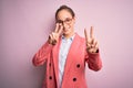 Young beautiful businesswoman wearing jacket and glasses over isolated pink background smiling looking to the camera showing Royalty Free Stock Photo