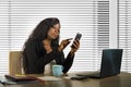 Young beautiful and busy black African American businesswoman using mobile phone working on desk with laptop computer at company Royalty Free Stock Photo