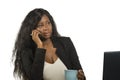 Young beautiful and busy black afro American businesswoman talking on mobile phone at office working with laptop computer drinking Royalty Free Stock Photo