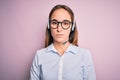 Young beautiful call center agent woman wearing glasses working using headset with serious expression on face Royalty Free Stock Photo