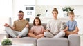 Father, mother and two children meditating with closed eyes while sitting in lotus pose together on sofa Royalty Free Stock Photo