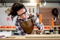 Young beautiful carpenter woman wearing safety glasses goggles and apron, using carpentry tools with wood plank to make wooden Royalty Free Stock Photo