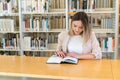 Young beautiful caucasian girl reading a book in the library Royalty Free Stock Photo