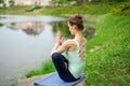 Young beautiful caucasian brunette girl doing yoga on a green lawn against the background of the river Royalty Free Stock Photo