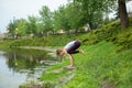 Young beautiful caucasian brunette girl doing yoga on a green lawn against the background of the river Royalty Free Stock Photo