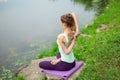 Young beautiful caucasian brunette girl doing yoga on a green lawn against the background of the river Royalty Free Stock Photo