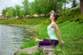 Young beautiful caucasian brunette girl doing yoga on a green lawn against the background of the river Royalty Free Stock Photo