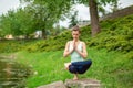 Young beautiful caucasian brunette girl doing yoga on a green lawn against the background of the river Royalty Free Stock Photo