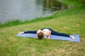 Young beautiful caucasian brunette girl doing yoga on a green lawn against the background of the river Royalty Free Stock Photo