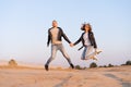 Young beautiful caucasian couple man and woman jumping holding hands on on sandy beach Royalty Free Stock Photo