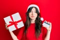 Young beautiful caucasian girl wearing christmas hat, holding a gift and credit card clueless and confused expression Royalty Free Stock Photo