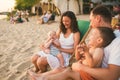 Young beautiful Caucasian happy family of four sitting together embracing at beach cafe in evening sunset. Theme family vacation Royalty Free Stock Photo