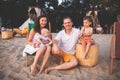 Young beautiful Caucasian happy family of four sitting together embracing at beach cafe in evening sunset. Theme family vacation Royalty Free Stock Photo