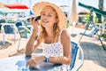 Young beautiful caucasian woman with blond hair smiling happy outdoors sitting at bar terrace listening to voice message on the Royalty Free Stock Photo