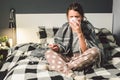 Young beautiful Caucasian woman has a cold, flu with high fever and heat at home in bed. The girl takes headache pills with a Royalty Free Stock Photo