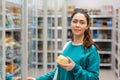 A young beautiful Caucasian woman holds a cheese in her hands and smiles sweetly.Shelves with food in the background. The concept Royalty Free Stock Photo