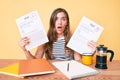 Young beautiful caucasian woman showing failed and passed exam sitting on the table in shock face, looking skeptical and Royalty Free Stock Photo