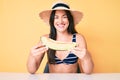 Young beautiful caucasian woman wearing bikini and hat holding slice of melon looking positive and happy standing and smiling with Royalty Free Stock Photo