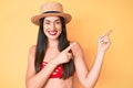 Young beautiful caucasian woman wearing bikini and hat smiling and looking at the camera pointing with two hands and fingers to Royalty Free Stock Photo