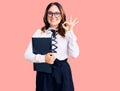 Young beautiful caucasian woman wearing business shirt and glasses holding folder doing ok sign with fingers, smiling friendly Royalty Free Stock Photo