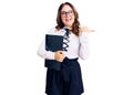 Young beautiful caucasian woman wearing business shirt and glasses holding folder pointing thumb up to the side smiling happy with Royalty Free Stock Photo