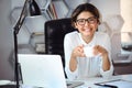 Young beautiful cheerful businesswoman drinking coffee, smiling at workplace in office. Royalty Free Stock Photo