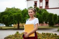 Young beautiful cheerful female student smiling, holding folders outdoors, park background. Royalty Free Stock Photo