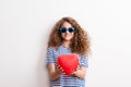 Young beautiful cheerful woman with sunglasses in studio, holding red heart. Royalty Free Stock Photo