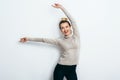 Young beautiful cheerful woman with hair bun wearing in jeans and sweater dancing and posing over white wall. Good mood. Hands up! Royalty Free Stock Photo