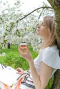 Beautiful young woman is drinking tea while sitting under a flowering tree in the garden. Royalty Free Stock Photo