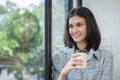 Young beautiful cheerful woman holding paper cup coffee smiling looking out window office. asian business woman relax time Royalty Free Stock Photo