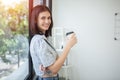 Young beautiful cheerful woman holding paper cup coffee smiling looking out window office. asian business woman relax time Royalty Free Stock Photo