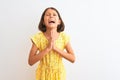 Young beautiful child girl wearing yellow floral dress standing over isolated white background begging and praying with hands Royalty Free Stock Photo