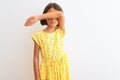 Young beautiful child girl wearing yellow floral dress standing over isolated white background covering eyes with arm, looking Royalty Free Stock Photo